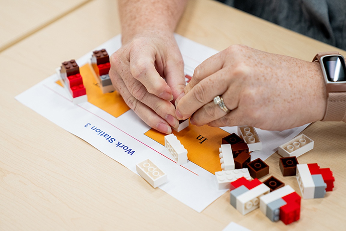 Close-up of hands assembling LEGO bricks over a work station instruction sheet