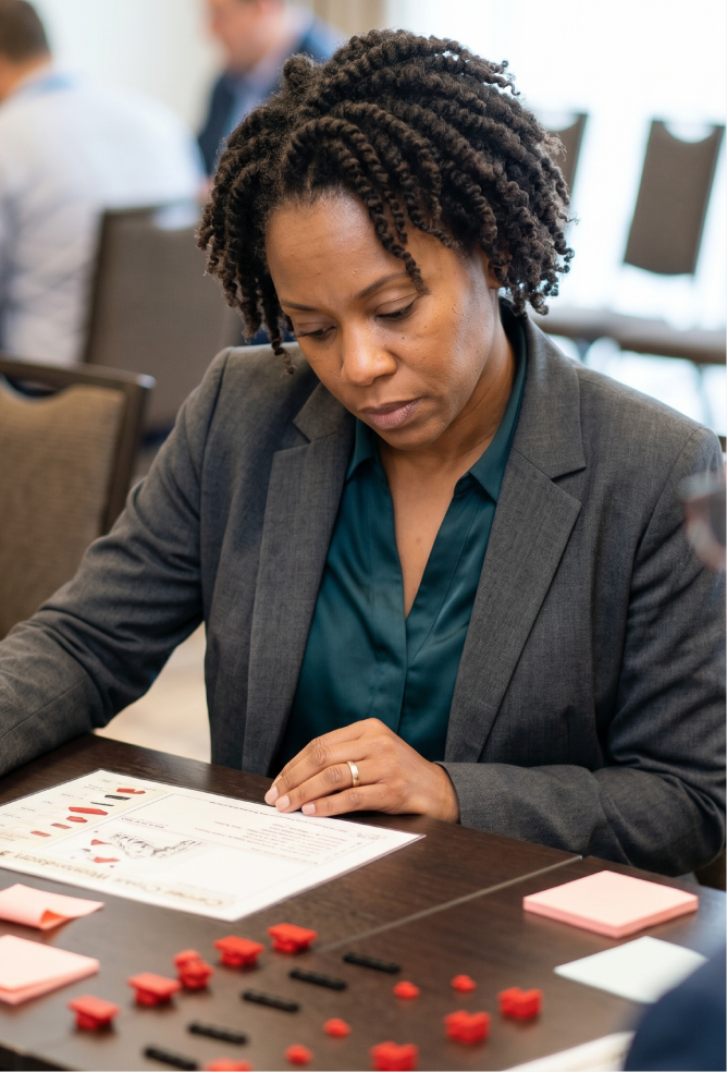 A participant studying a printed work instruction sheet beside sorted red and black LEGO bricks