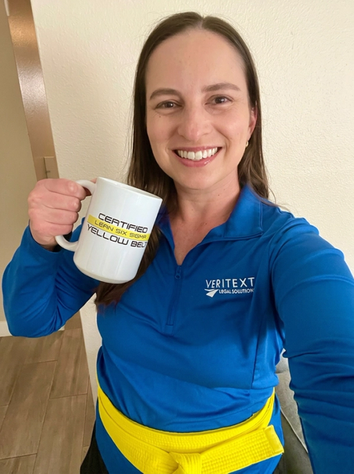 A Veritext employee wearing her yellow belt and holding a 'Certified Lean Six Sigma Yellow Belt' Coffee Mug