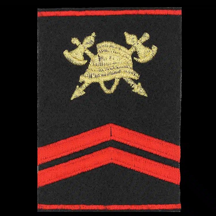 Black epaulet cover embroidered with a gold crossed axe and helmet crest above two red chevrons.