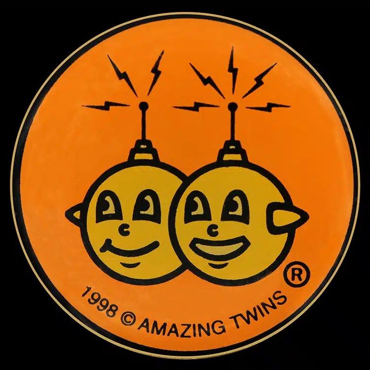 Round orange silkscreened lapel pin with a printed cartoon character design.