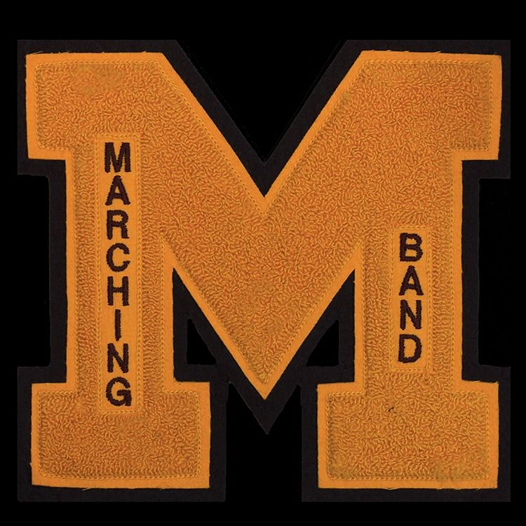 Gold chenille block letter M on a black felt backing, with small black embroidered words running down each leg.