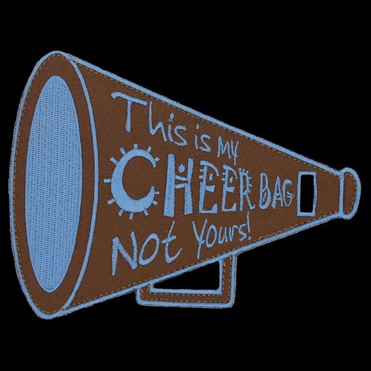 Die-cut embroidered bag tag shaped like a brown megaphone with light blue hand-lettered words.