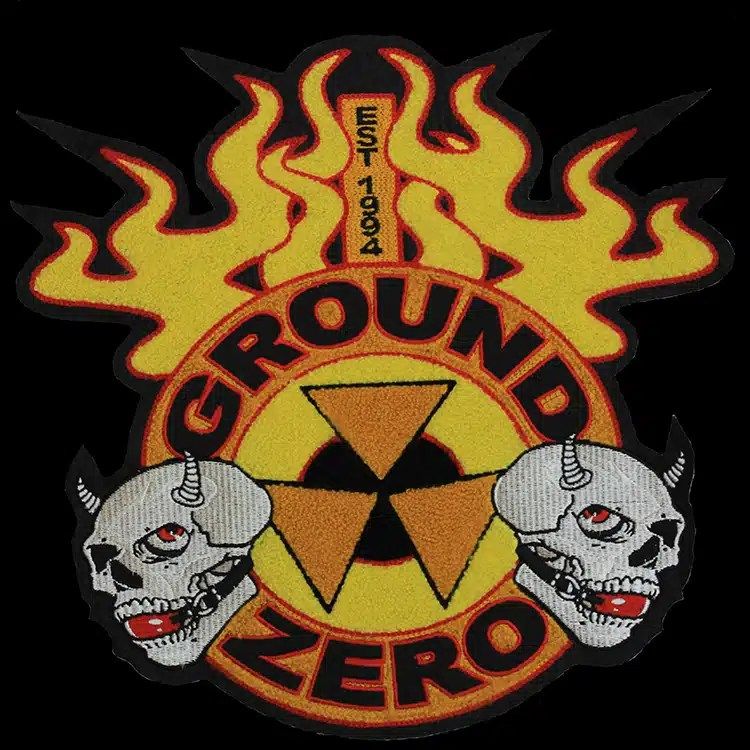 Large die-cut back patch with yellow and orange chenille flames and a chenille radiation symbol, two embroidered grey skulls and black block lettering around a ring.