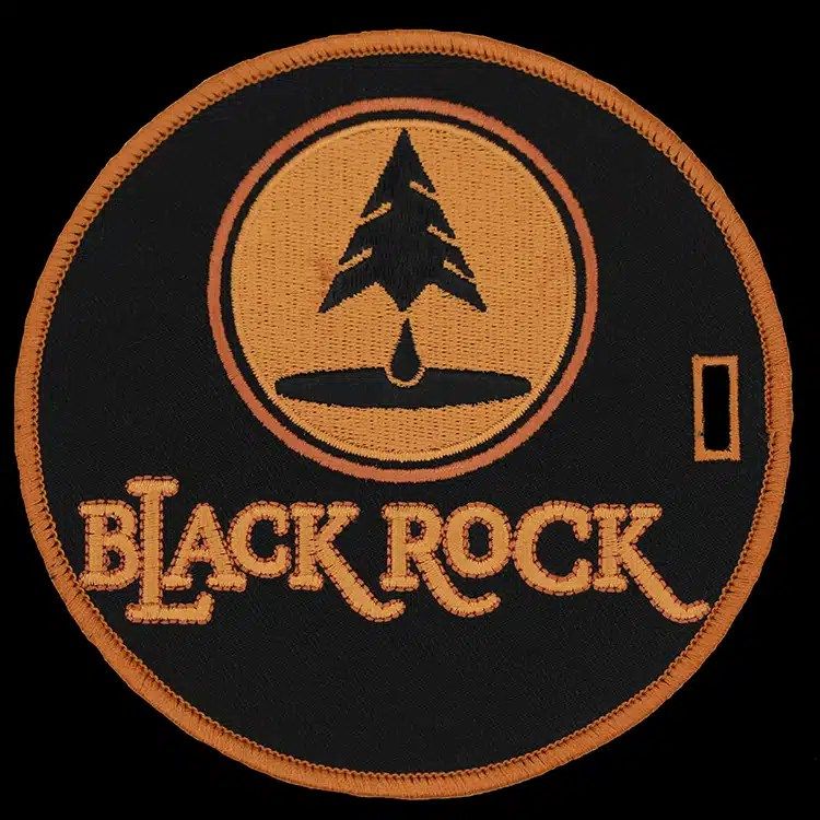 Round black embroidered bag tag with an orange tree-and-drop emblem and orange lettering.
