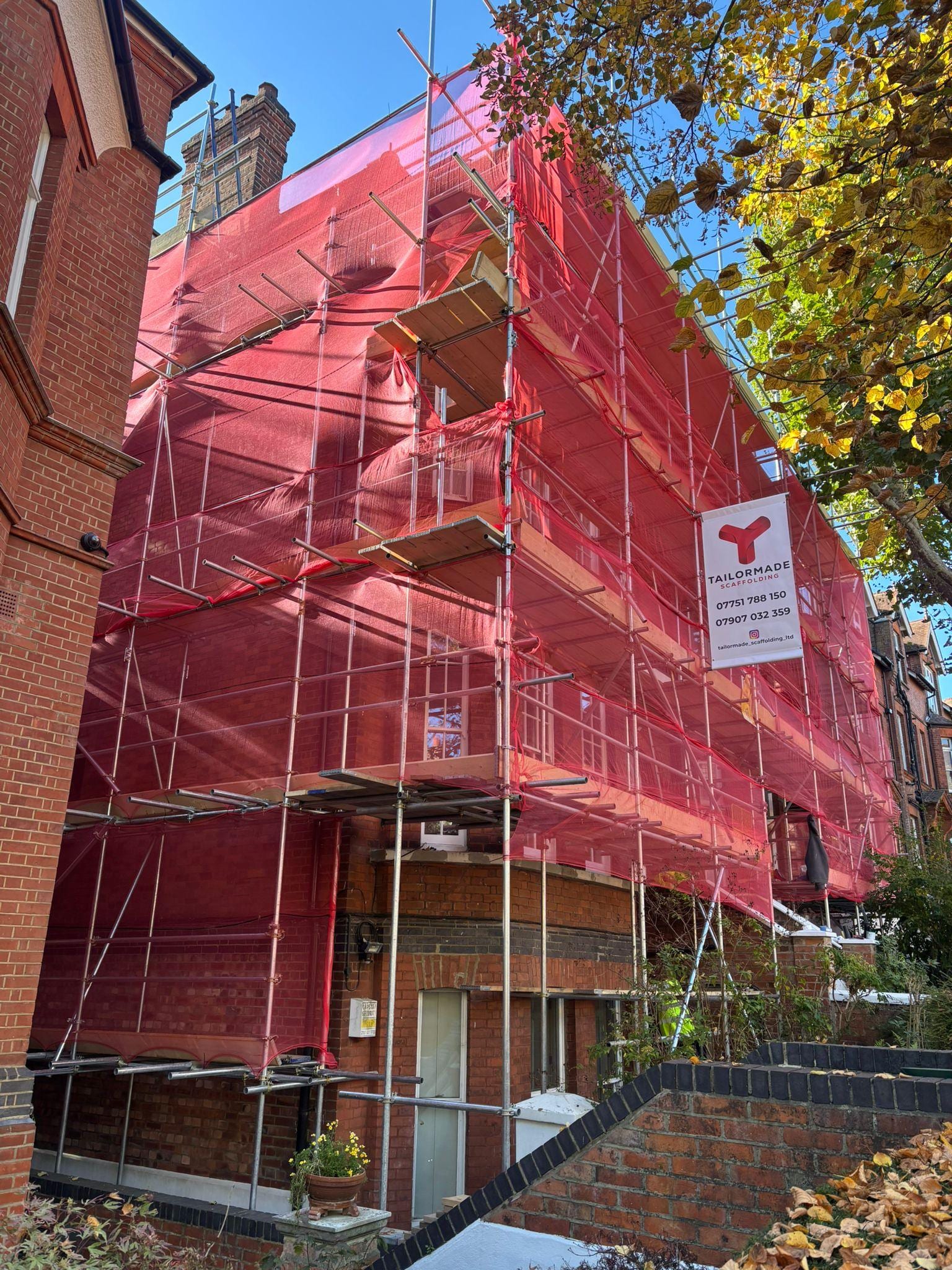 Scaffolding with red debris netting and a Tailormade Scaffolding sign on a tall period house