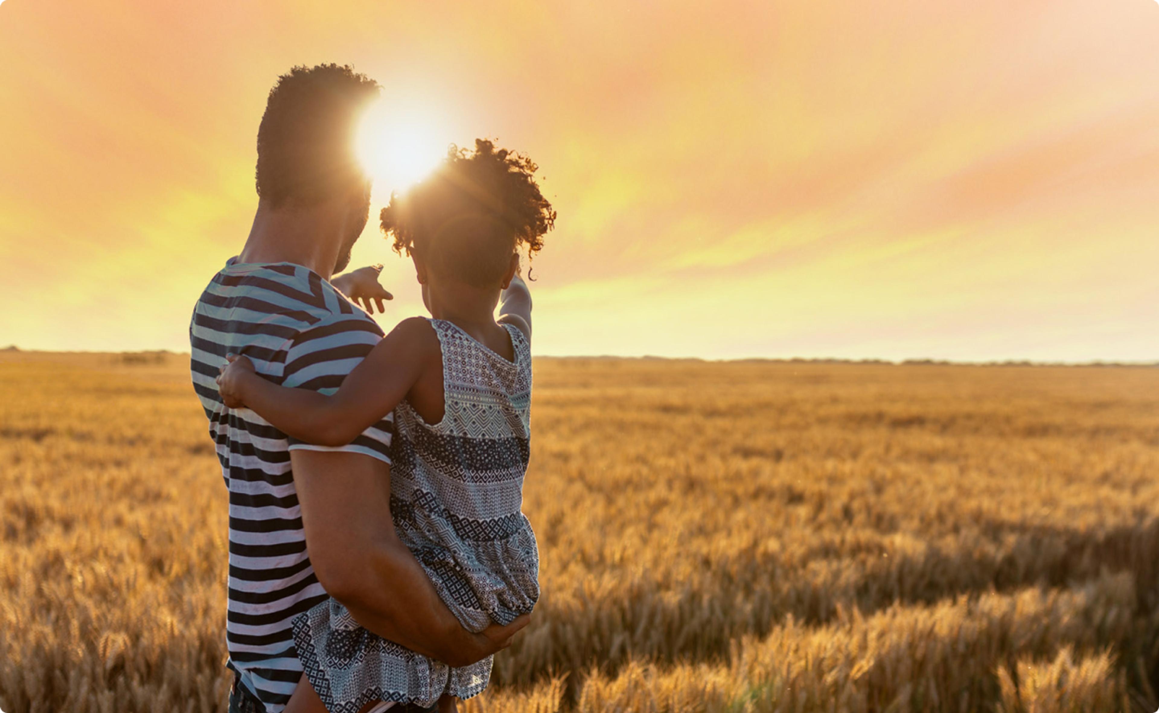 Man holding a child watching the sunset in a field