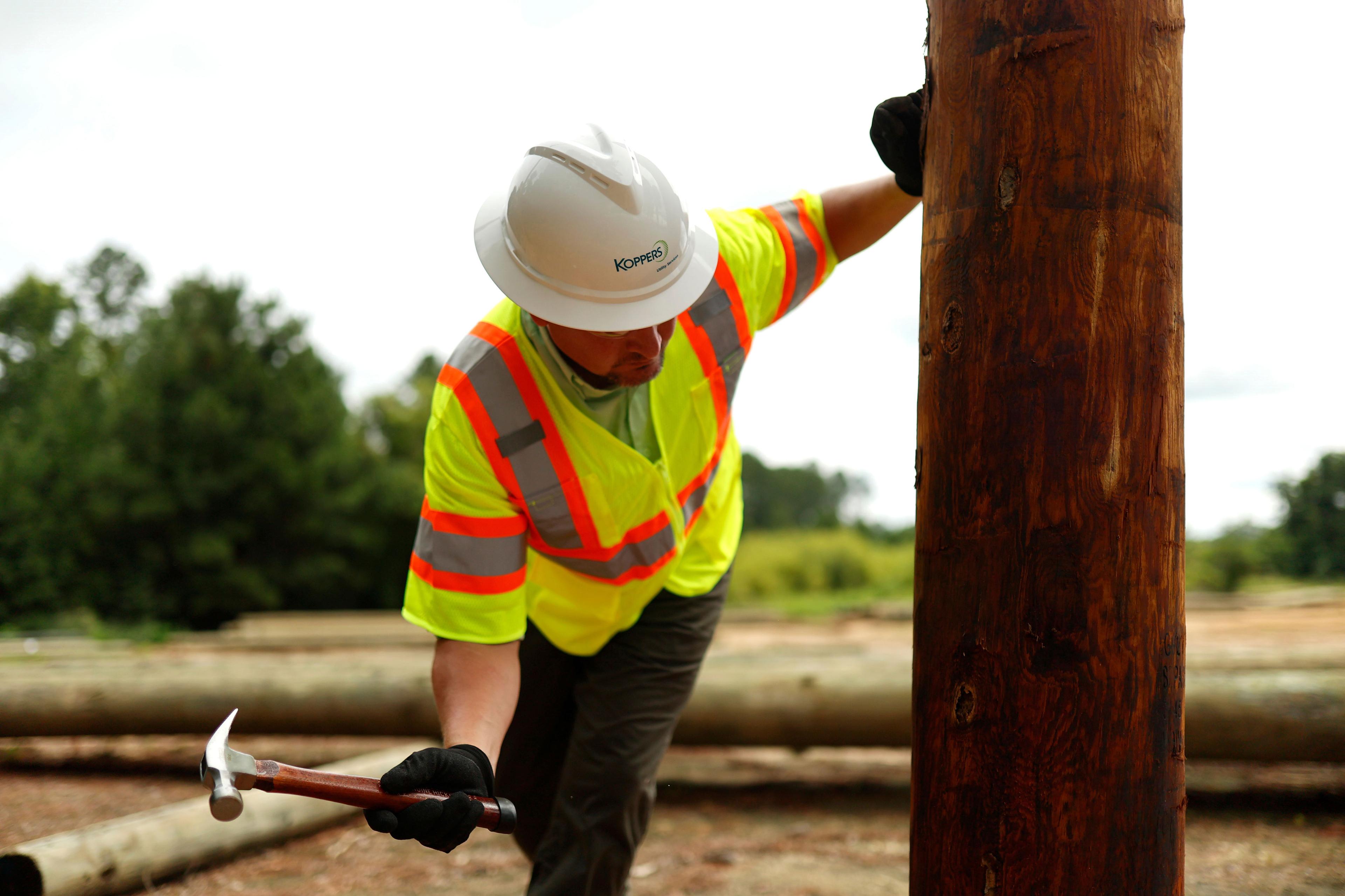 Koppers employee with a hammer holding onto a utility pole