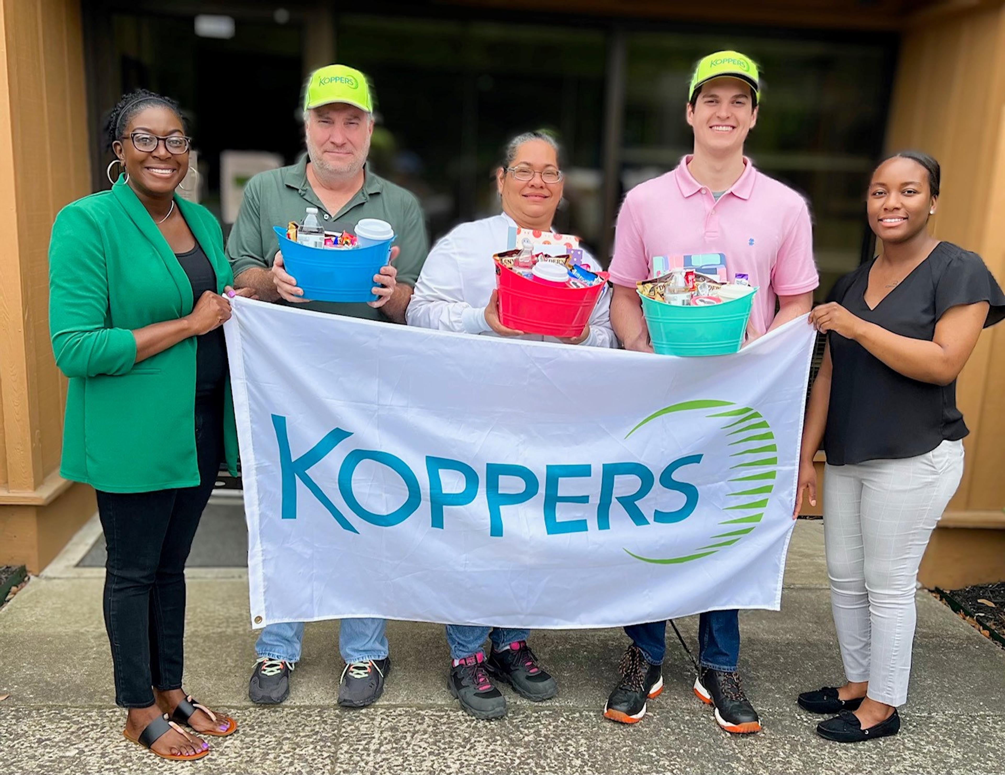 People posing with a Koppers banner