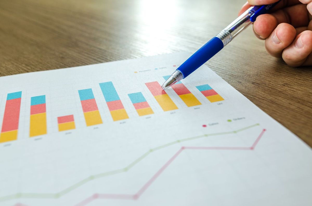 Hand holding a pen over a printed bar chart, reading market data