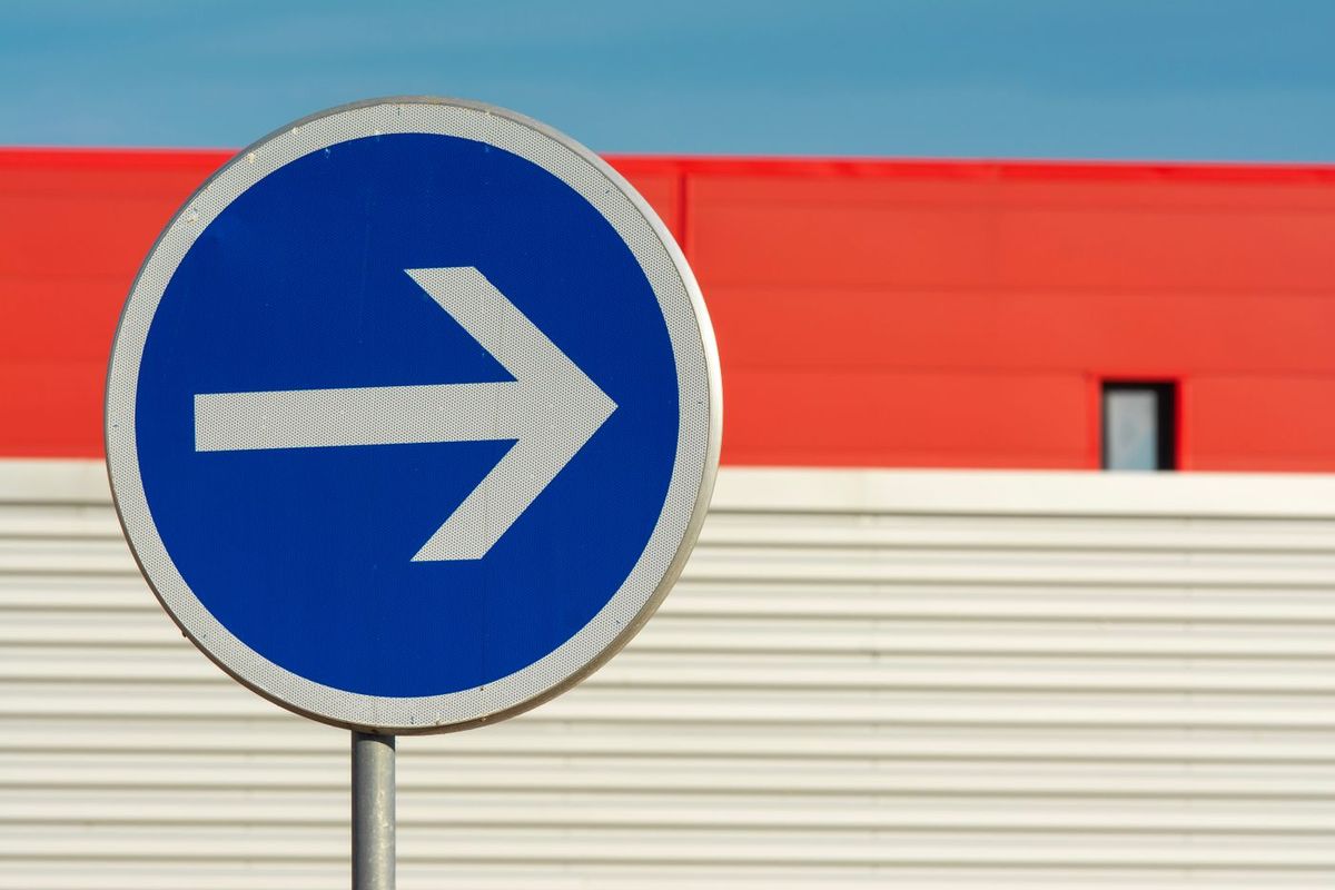 Round blue road sign with a white arrow showing the direction to take