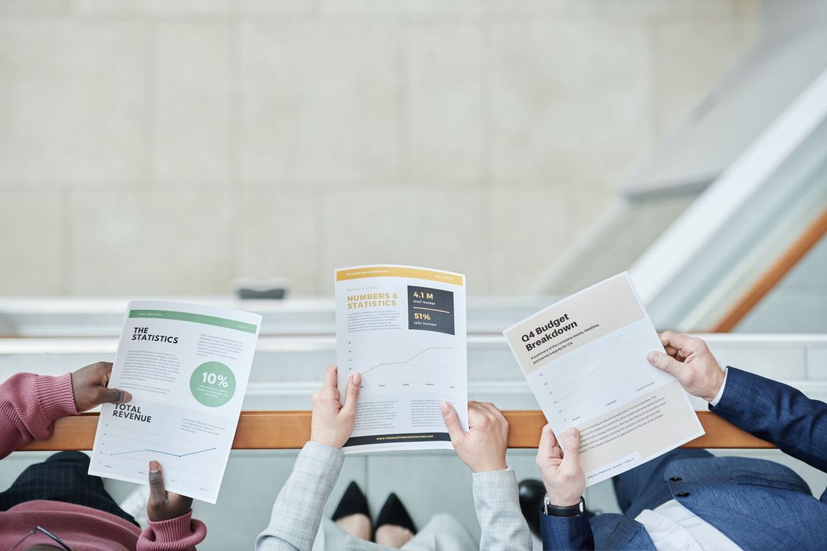 Three people comparing printed reports side by side around a table