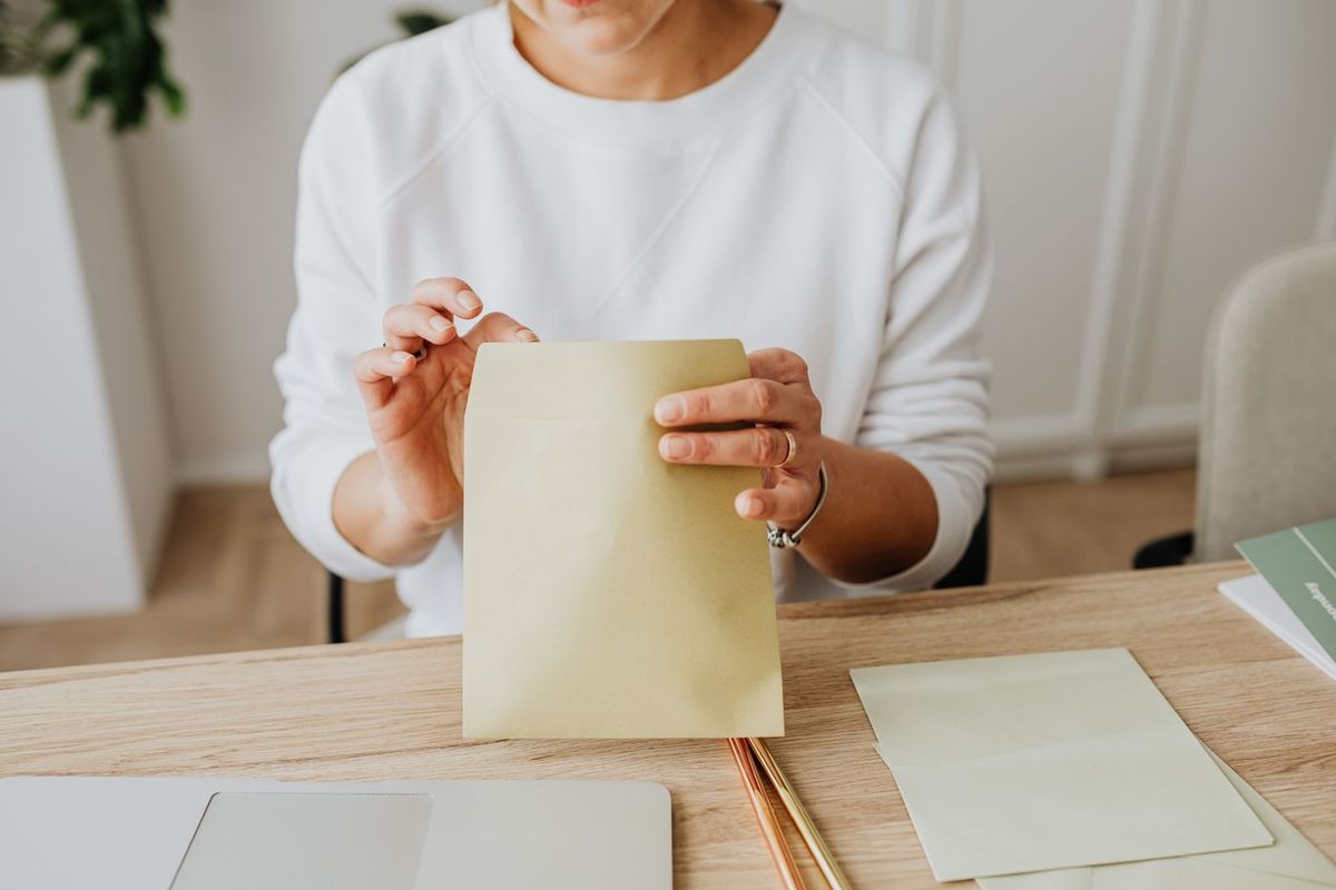 Woman slipping a document into an envelope at her desk, laptop in front of her