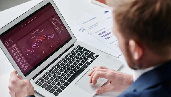 Geschäftsführer prüft ein Analyse-Dashboard auf dem Laptop, daneben gedruckte Berichte