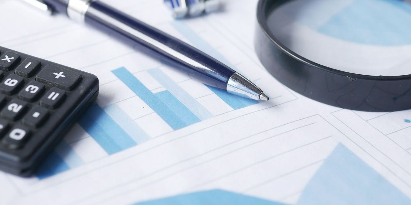 Magnifying glass, calculator and pen on printed bar charts