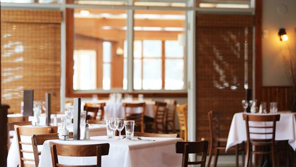 Warmes Interieur eines europaeischen Restaurants mit gedeckten Tischen fuer den Service