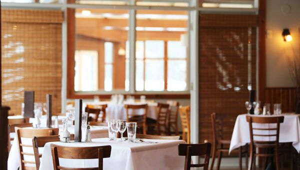 Warmes Interieur eines europaeischen Restaurants mit gedeckten Tischen fuer den Service
