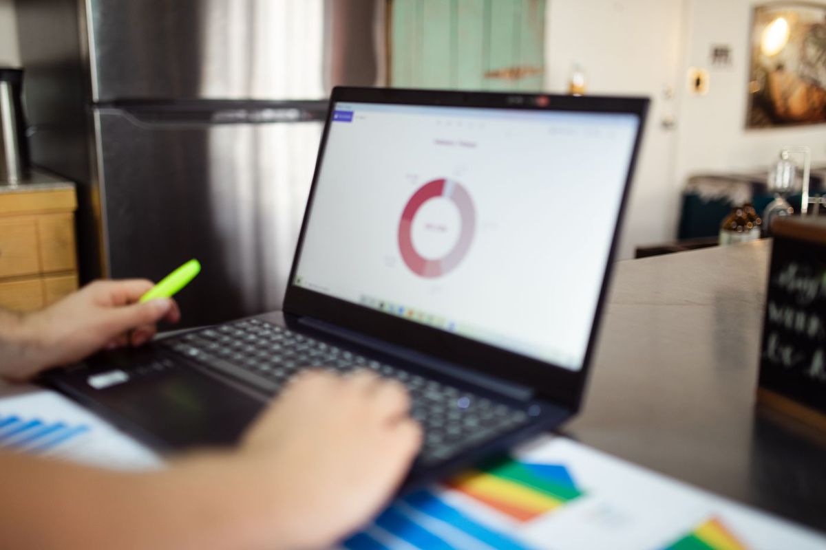 Mains sur un ordinateur portable affichant un graphique en anneau, un surligneur à la main et un graphique imprimé à côté