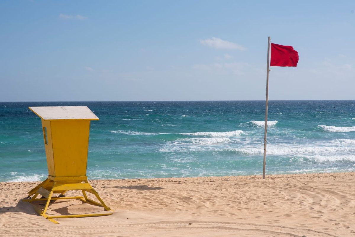 Drapeau rouge sur une plage, à côté d'un poste de surveillance jaune