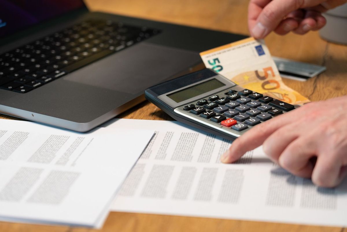 Calculator, a 50-euro note and printed documents next to a laptop