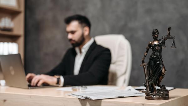 Anwalt am Laptop an einem Schreibtisch, im Vordergrund eine Justitia-Statuette