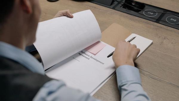 Person reading a software development agreement, pen in hand