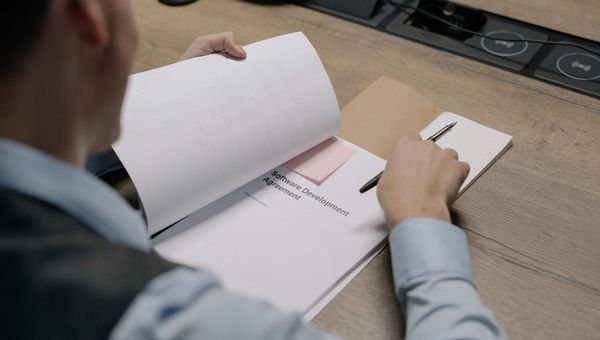 Person reading a software development agreement, pen in hand