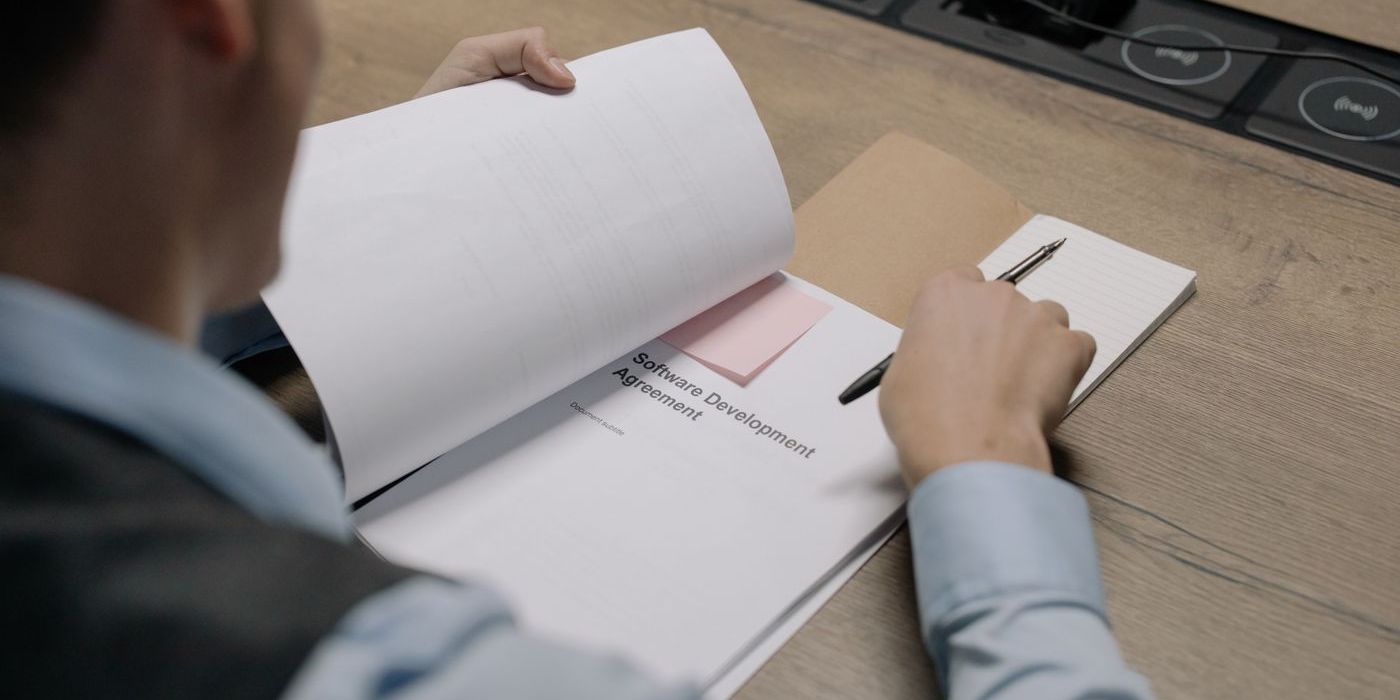 Person liest einen Softwareentwicklungsvertrag, Stift in der Hand