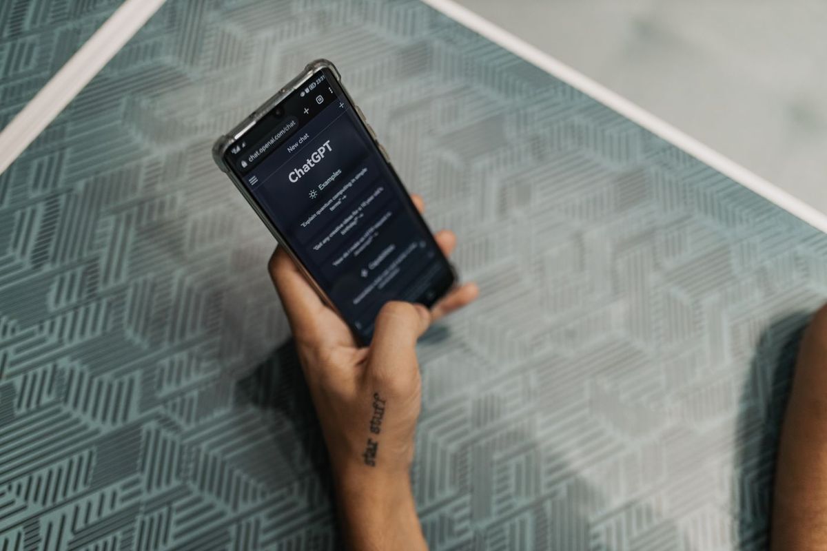 Hand hält ein Telefon mit einem KI-Chatassistenten auf dem Bildschirm