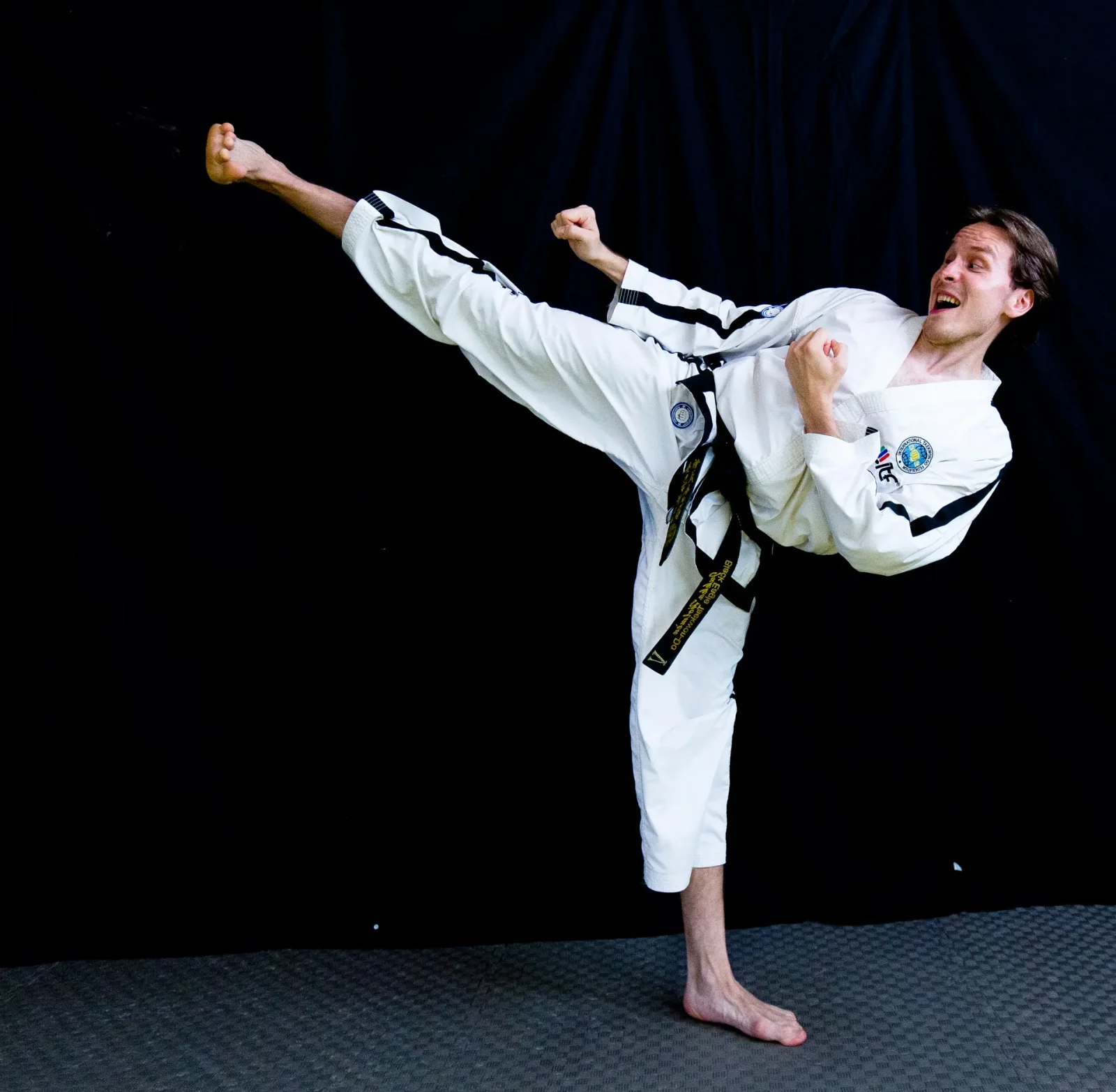 Taekwon-Do-harrastaja sivupotkuasennossa mustaa taustaa vasten