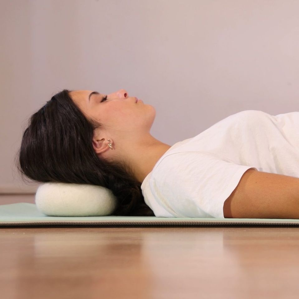 Femme allongée sur un tapis, la nuque posée sur le galet Dungha