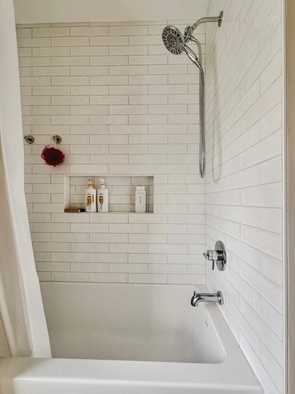 White subway-tile tub surround with a recessed shelf and handheld shower head