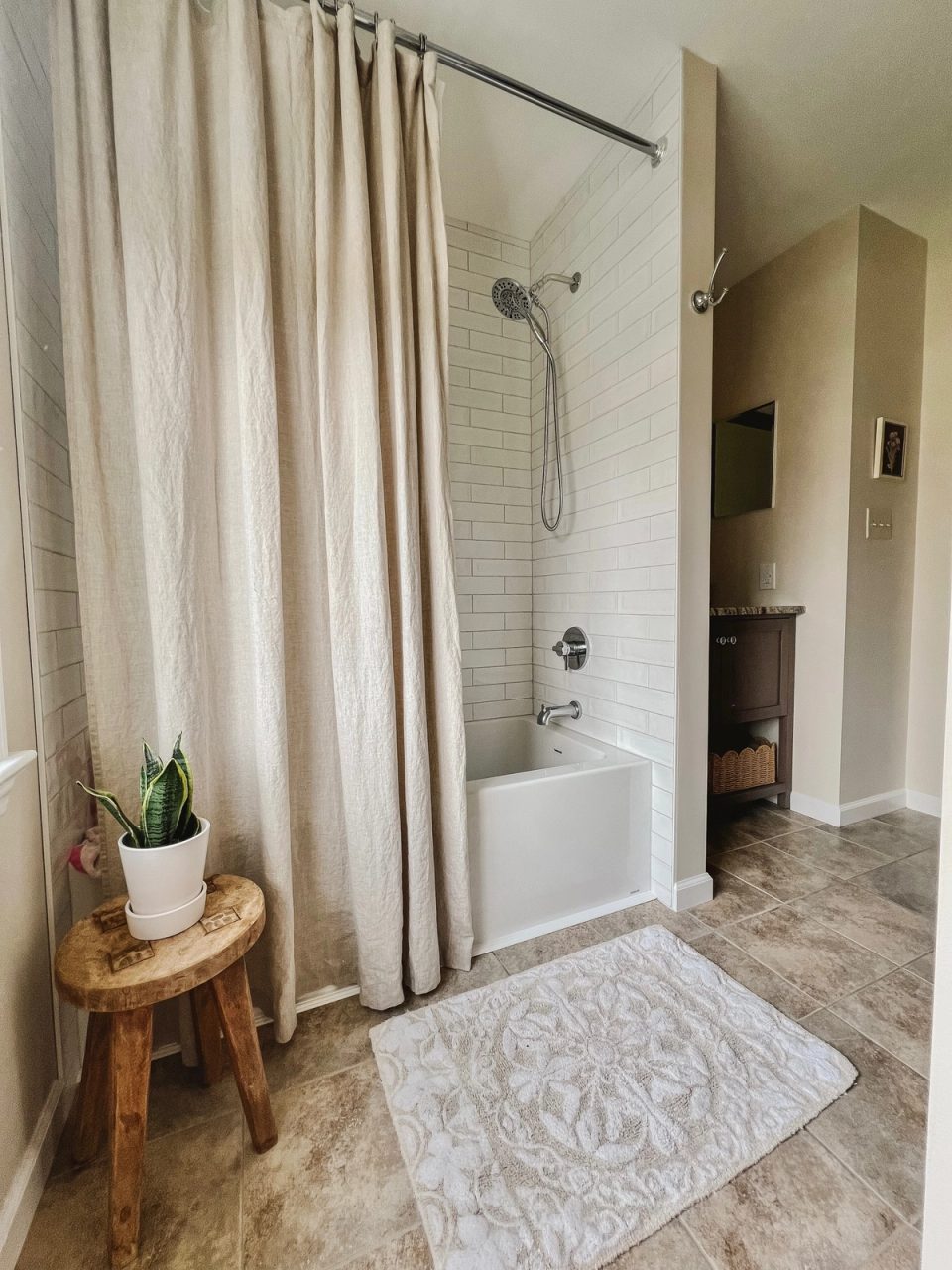 Refreshed shower with a linen curtain, patterned bath mat and plant on a wood stool