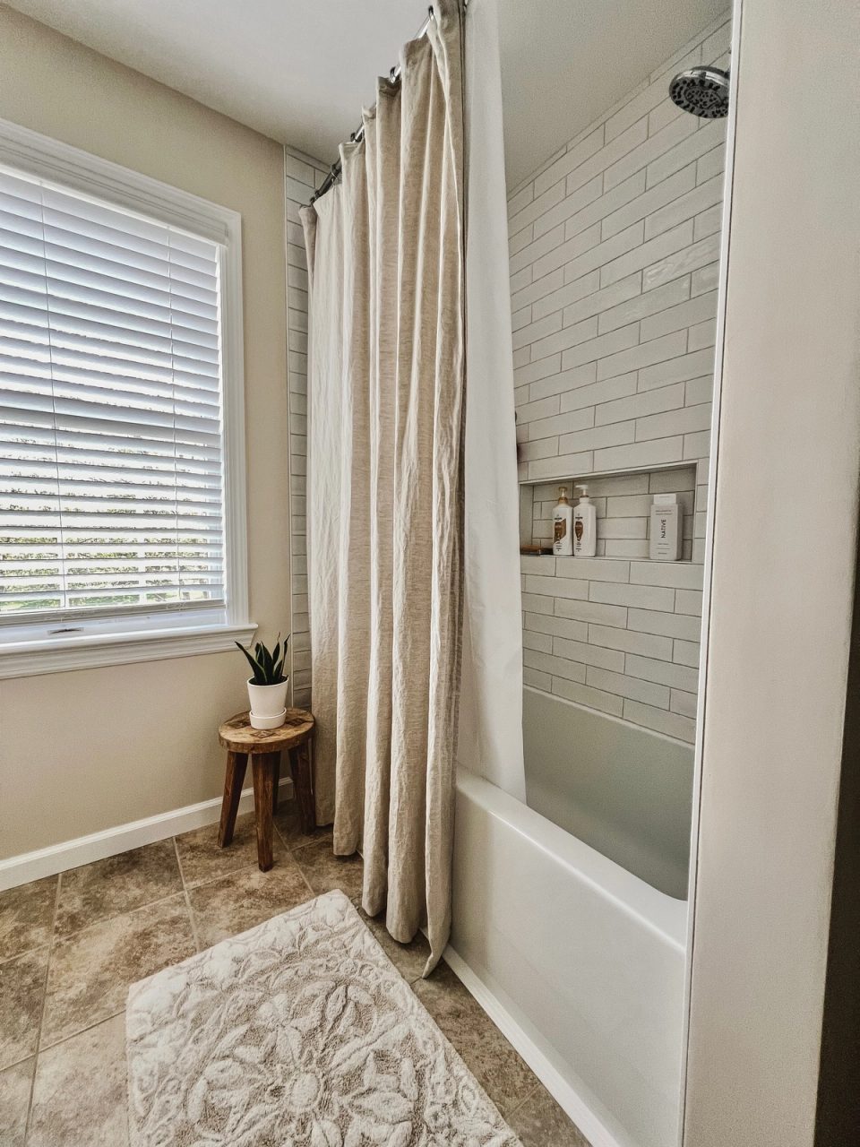White subway-tile shower with an extra-long linen curtain beside the bathroom window
