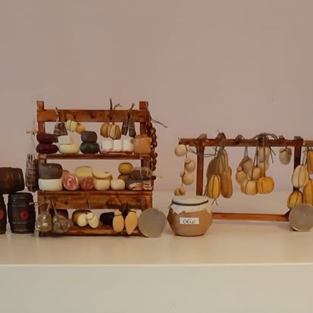 Angolo di salumeria con scaffale di formaggi e salumi accanto a una rastrelliera di aglio e cipolle