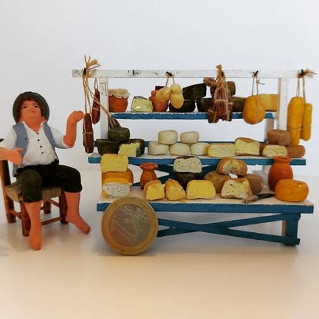 Bancarella blu con formaggi e salumi in mostra e il venditore seduto accanto