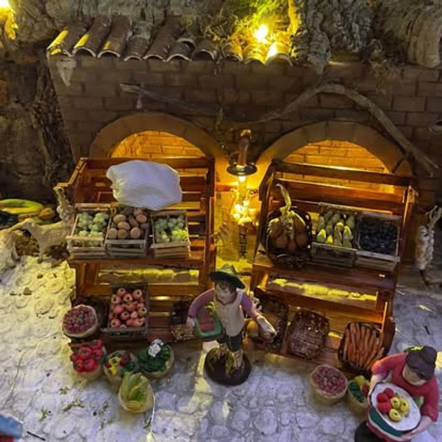 Bottega con due archi in muratura, banchi di frutta e verdura illuminati da una lanterna