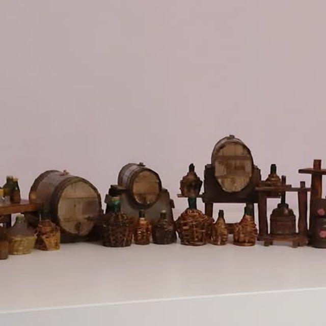 Scena di cantina con botti di diverse misure, damigiane e ceste di bottiglie