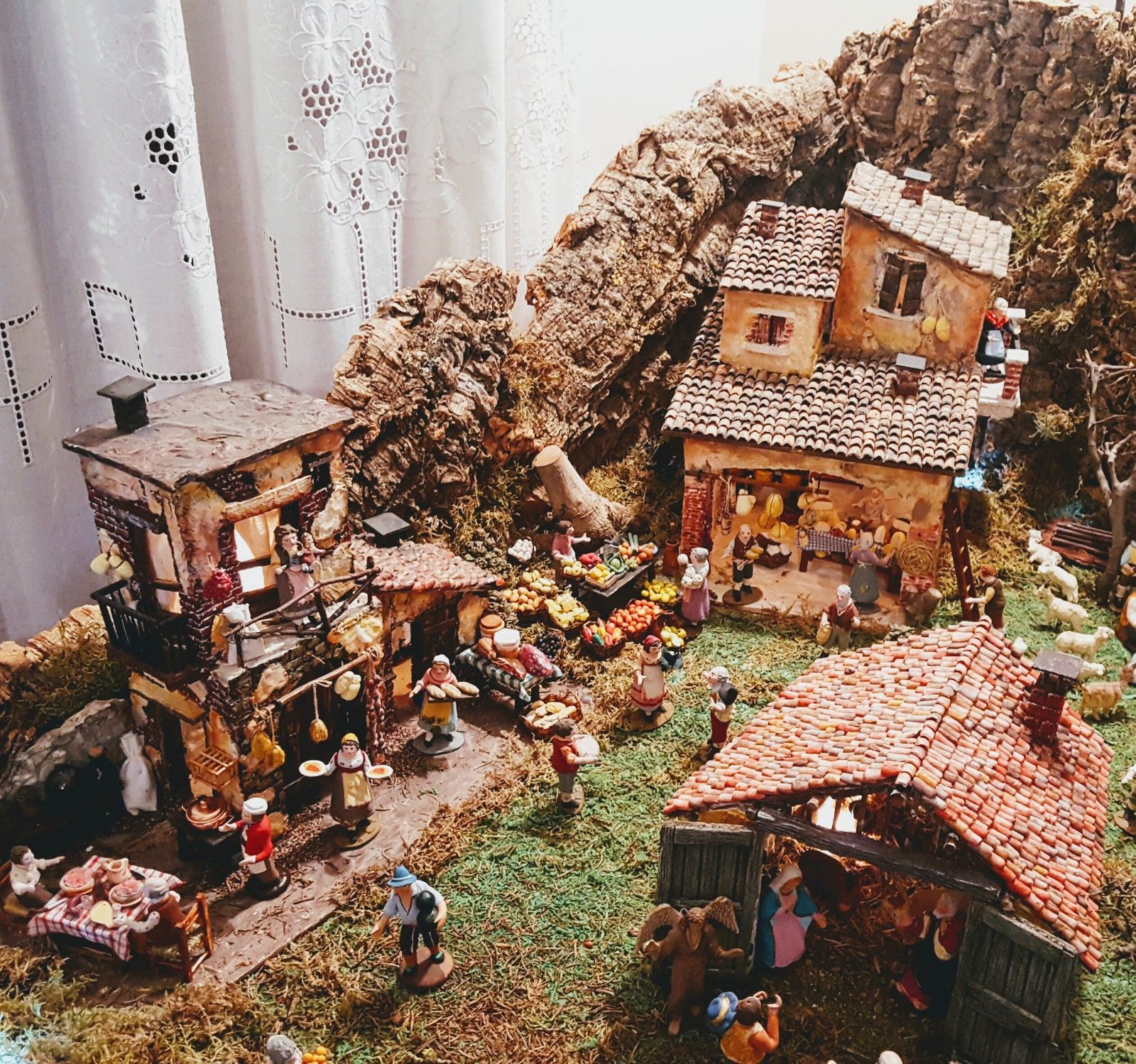 Presepe completo con borgo di casette, mercato animato e capanna della Natività, ambientato tra scogli in sughero