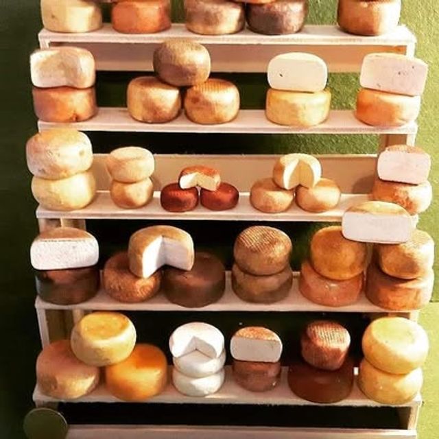 Scaffale a cinque ripiani con forme di formaggio di diverse dimensioni e colori