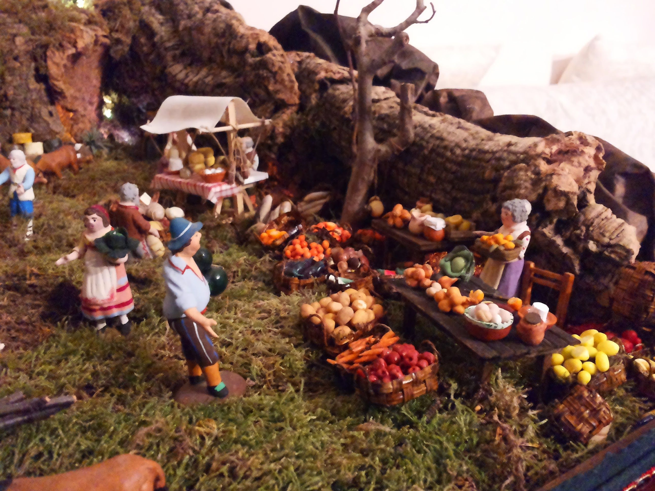 Scena di mercato in un presepe con banchi di frutta e verdura, venditori e clienti tra gli scogli