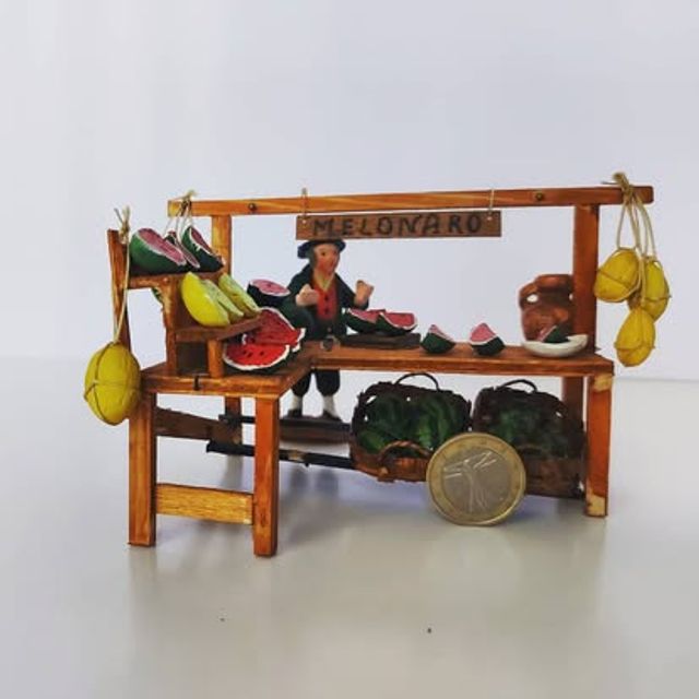 Bancarella del melonaro con insegna, angurie tagliate e meloni appesi