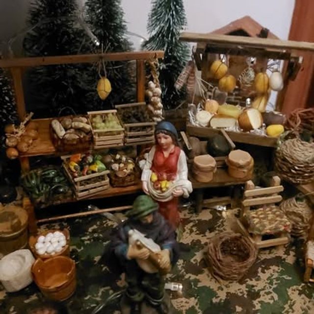 Bancarella di frutta e verdura tra alberelli, con una venditrice e un pastore con fisarmonica
