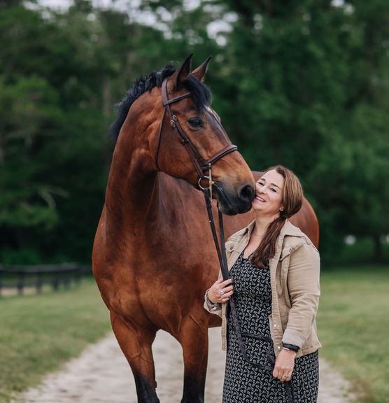Woman standing next to a horse, horse is nuzzling woman's cheek
