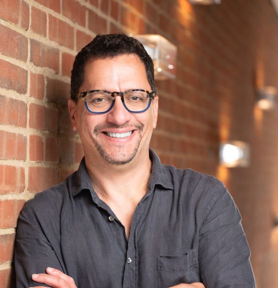 Man wearing glasses and a dark grey shirt standing next to a brick wall