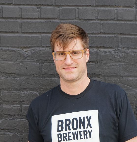 Man with glasses and a Bronx Brewery t-shirt standing in front of a grey brick wall
