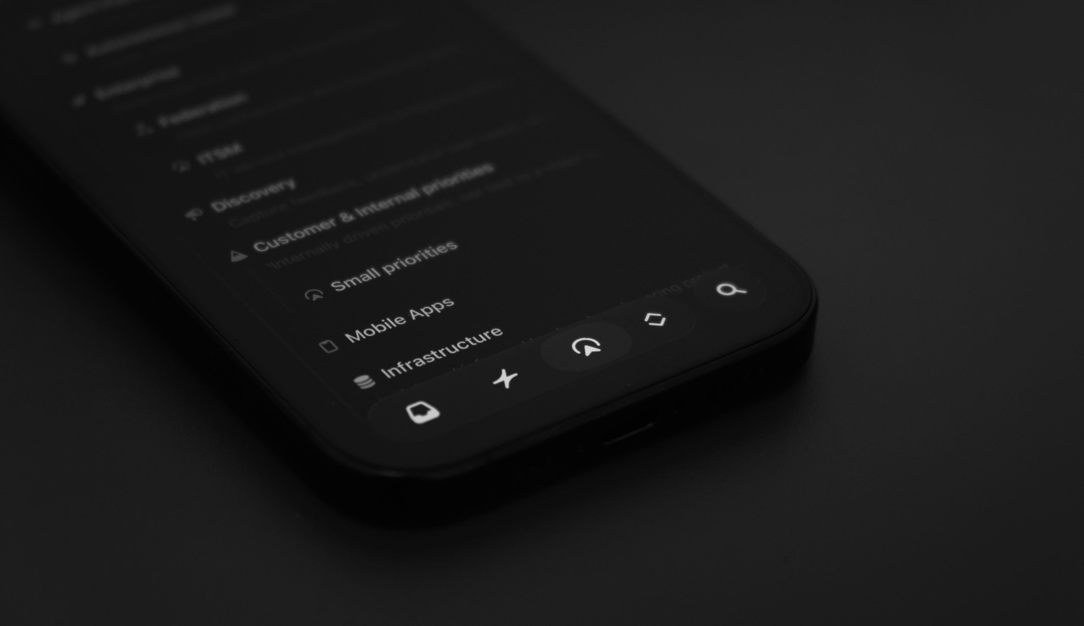 Close-up of a smartphone showing the Linear app interface, with a blurred list of projects and navigation icons along the bottom.