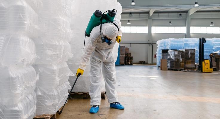 A technician in a protective suit treating the floor of a warehouse