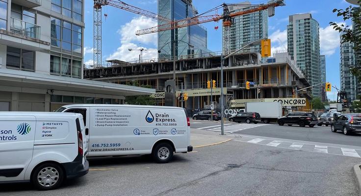 A Drain Express service van parked on a city street beside a high-rise construction site