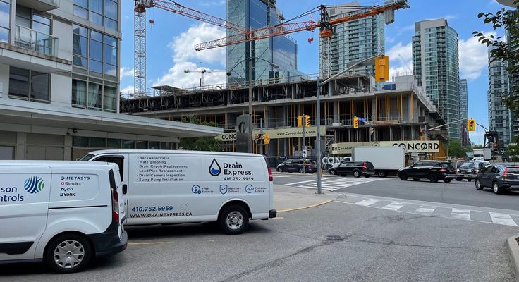 A Drain Express service van parked on a city street beside a high-rise construction site